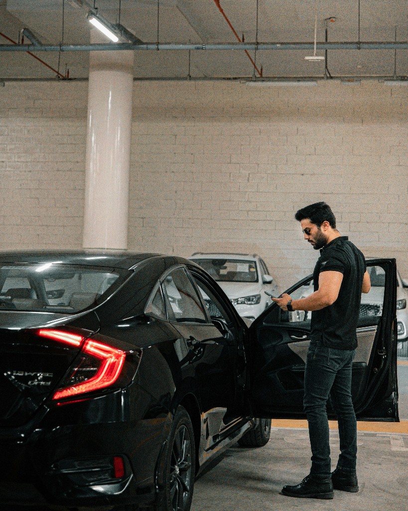 Fleet inspector beside a vehicle in a garage, reviewing details on a smartphone